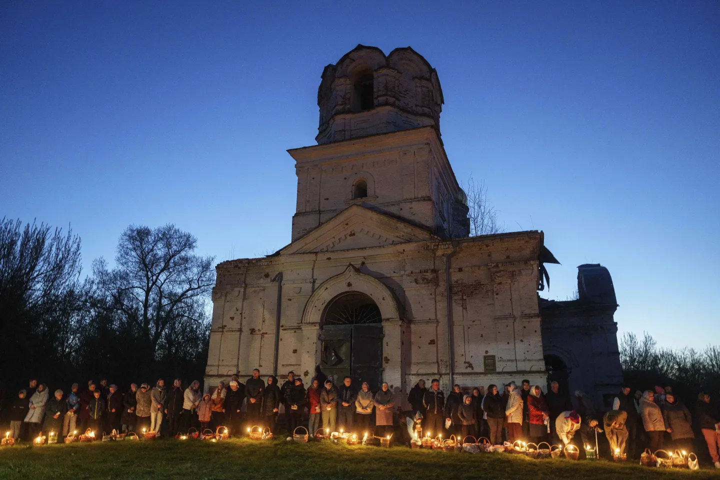 Люди стоять у черзі, щоб освятити свої пасхальні кошики перед церквою, зруйнованою внаслідок боїв між російсько-українськими військами, під час святкування православного Великодня в селі Лукашівка, Україна, у неділю, 20 квітня 2025 року.